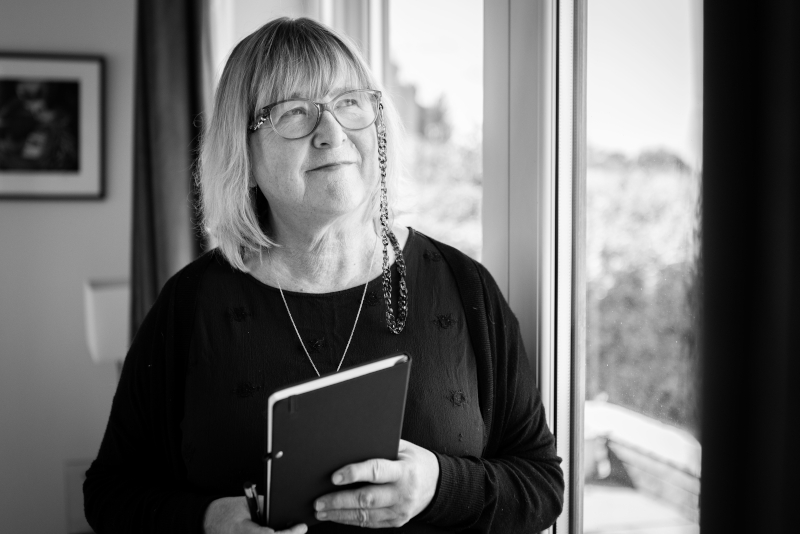 Gill looking in to the distance holding a book, photograph.